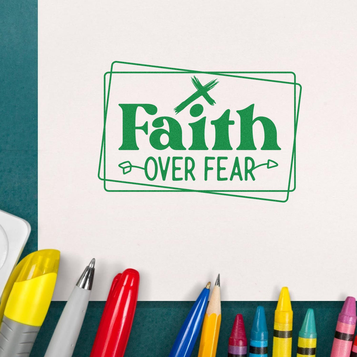 Green Faith Over Fear stamp seal on white paper, with crossed lines and colorful pens along the bottom.