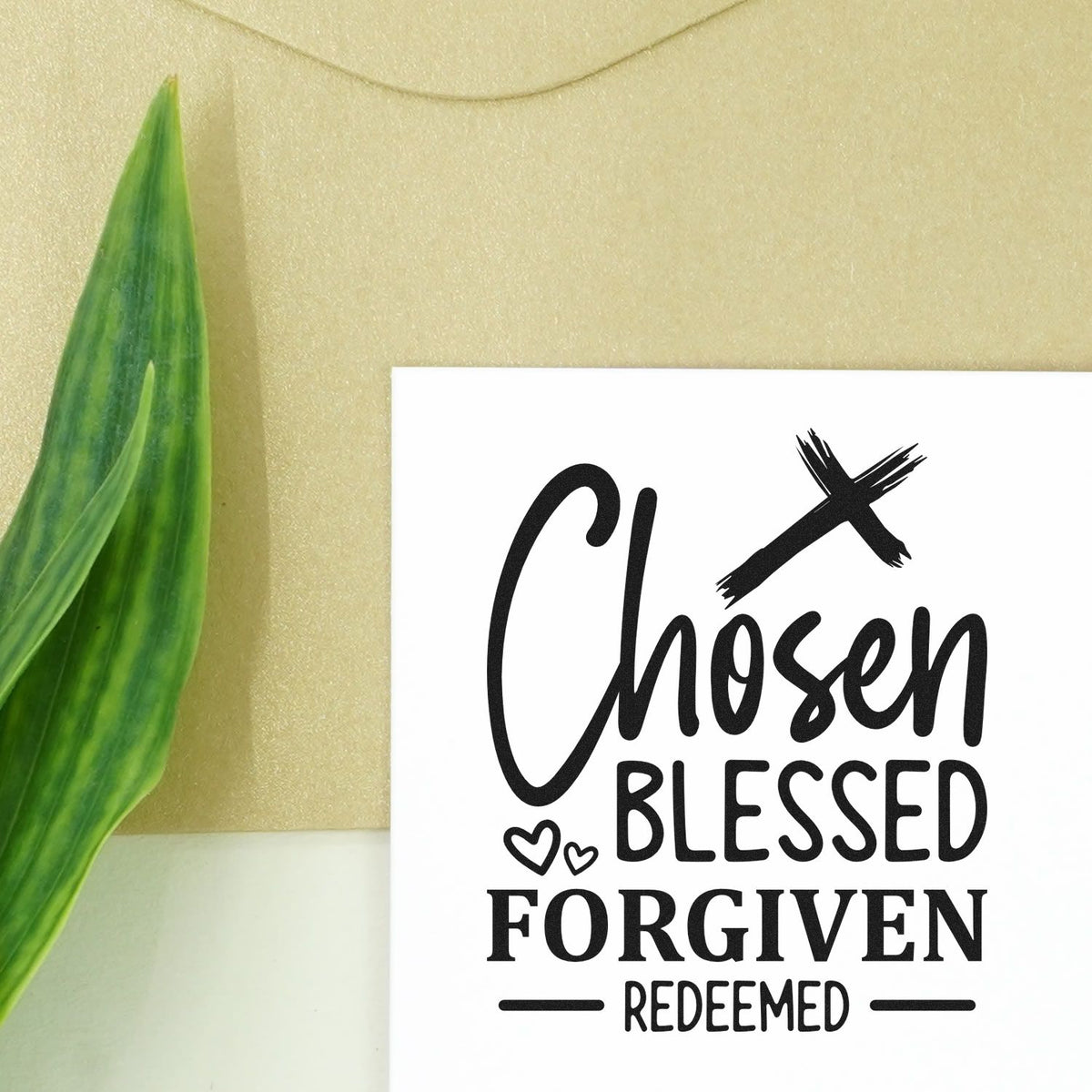 White rubber stamp seal with black Chosen Blessed Forgiven Redeemed lettering, green leaf, and beige background.