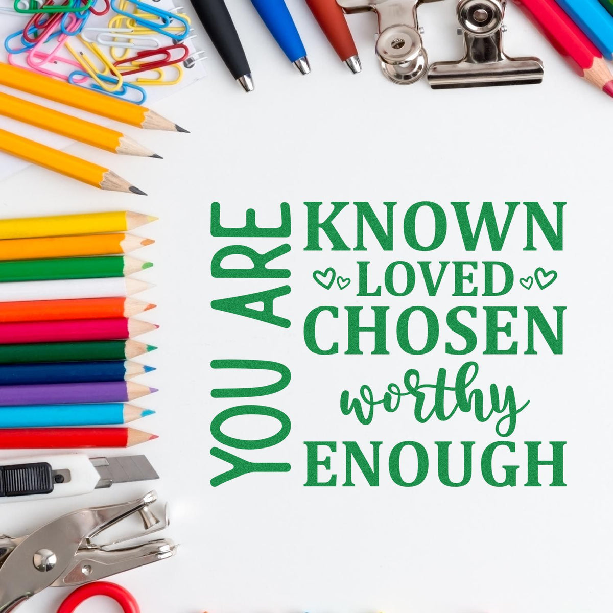 Green inspirational stamp and seal reading You are known, loved, chosen, worthy, enough, with colorful pencils and office supplies.