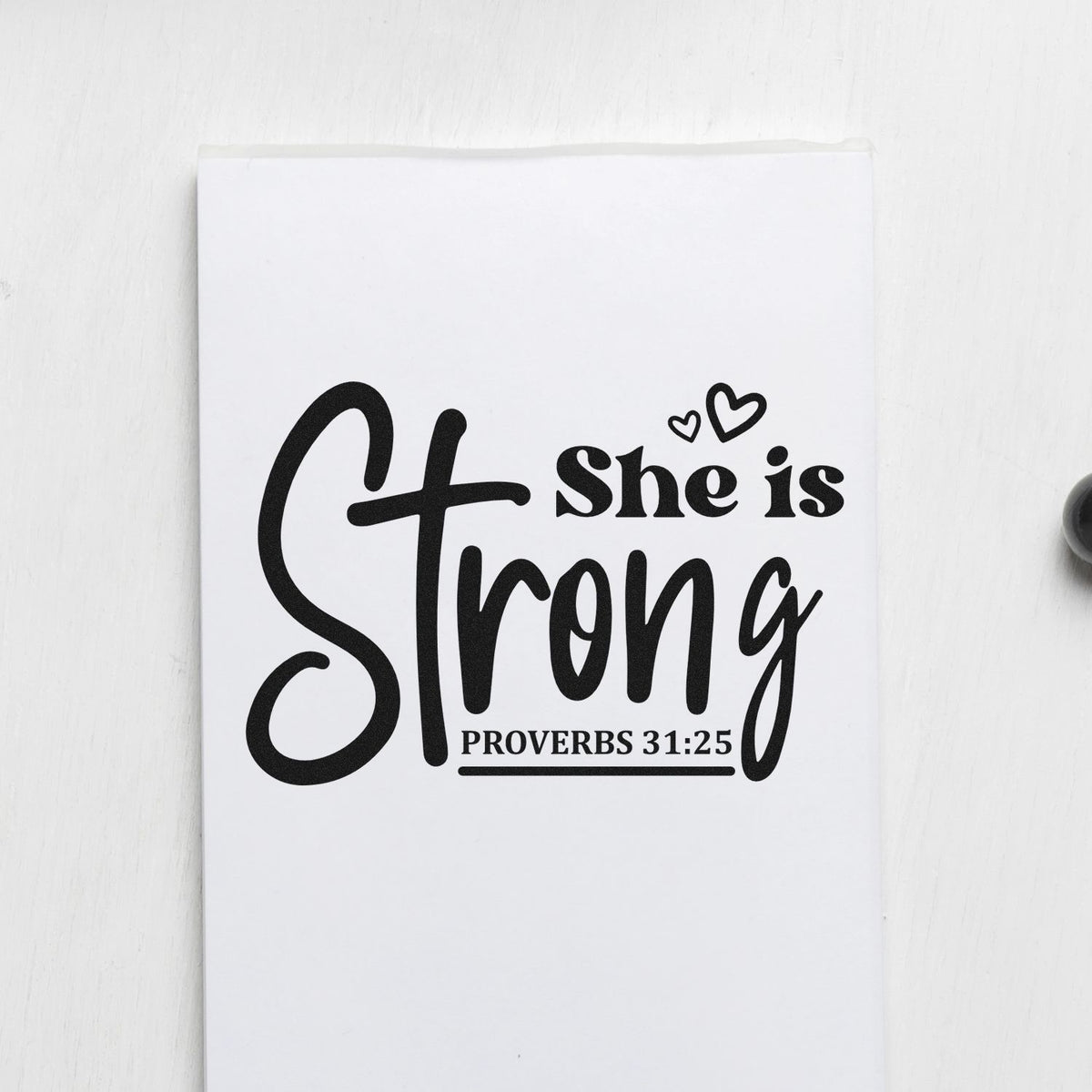 Black custom stamp and seal reading She is Strong with Proverbs 31:25 and heart accents on white.