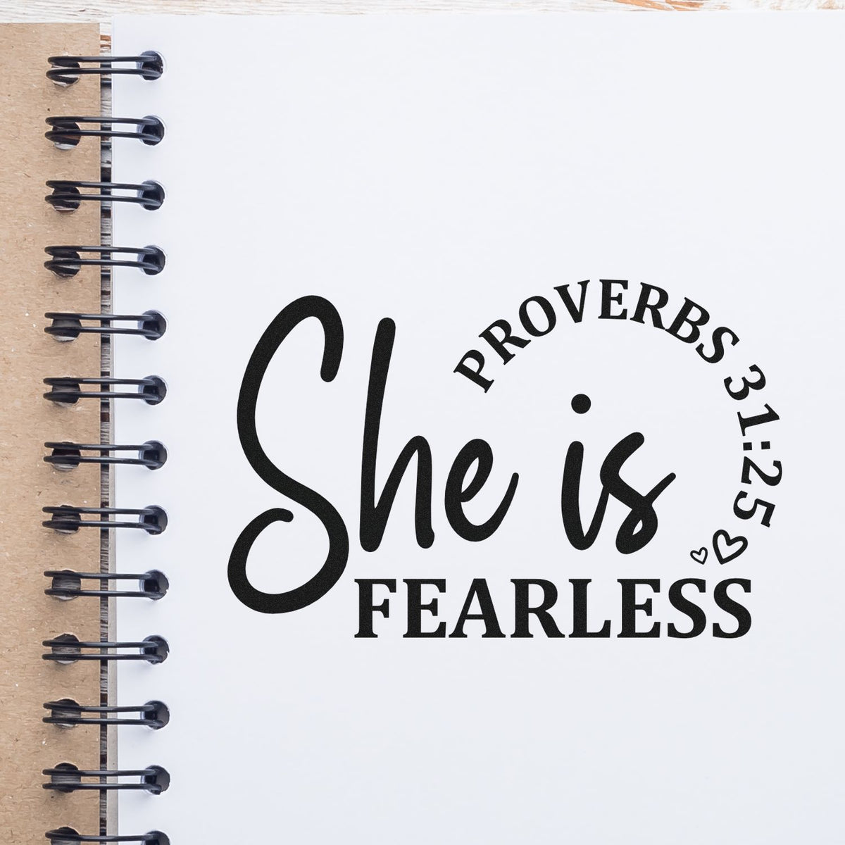Vintage Pro She Is Fearless Script Premium Wooden Stamp imprint stamped in black ink. Large "She is" script sits above "Fearless," with curved Proverbs 31:25 text and small hearts.