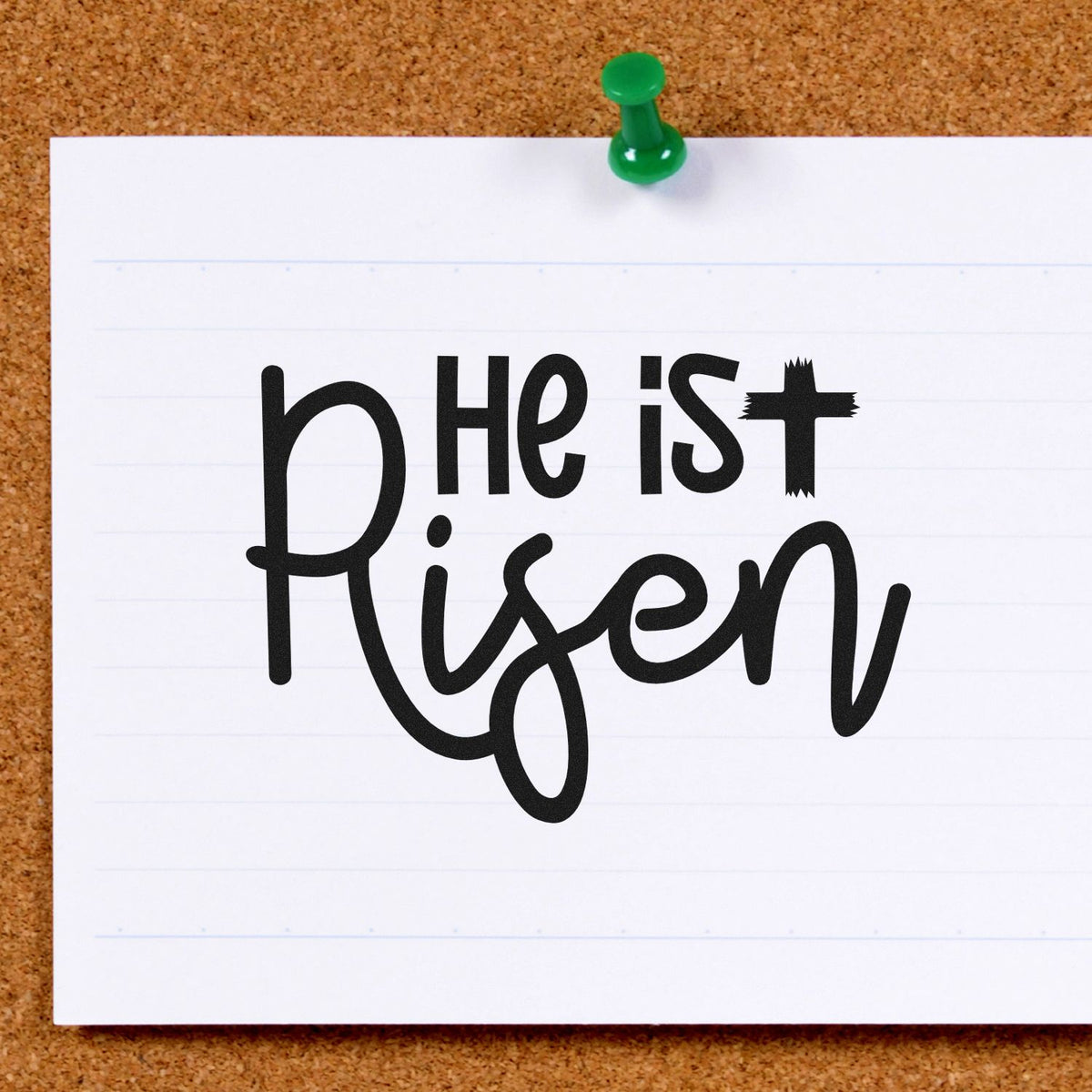 Black "He is Risen" stamp and seal design on white paper, pinned with a green pushpin on corkboard.