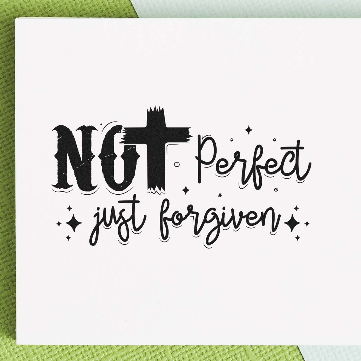 Black decorative stamp and seal design reading Not Perfect, Just Forgiven on white paper with sparkles over a green textured background.