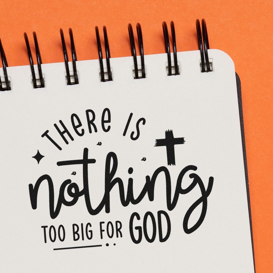 Black stamp and seal quote on white spiral notebook, orange background: There is nothing too big for God.