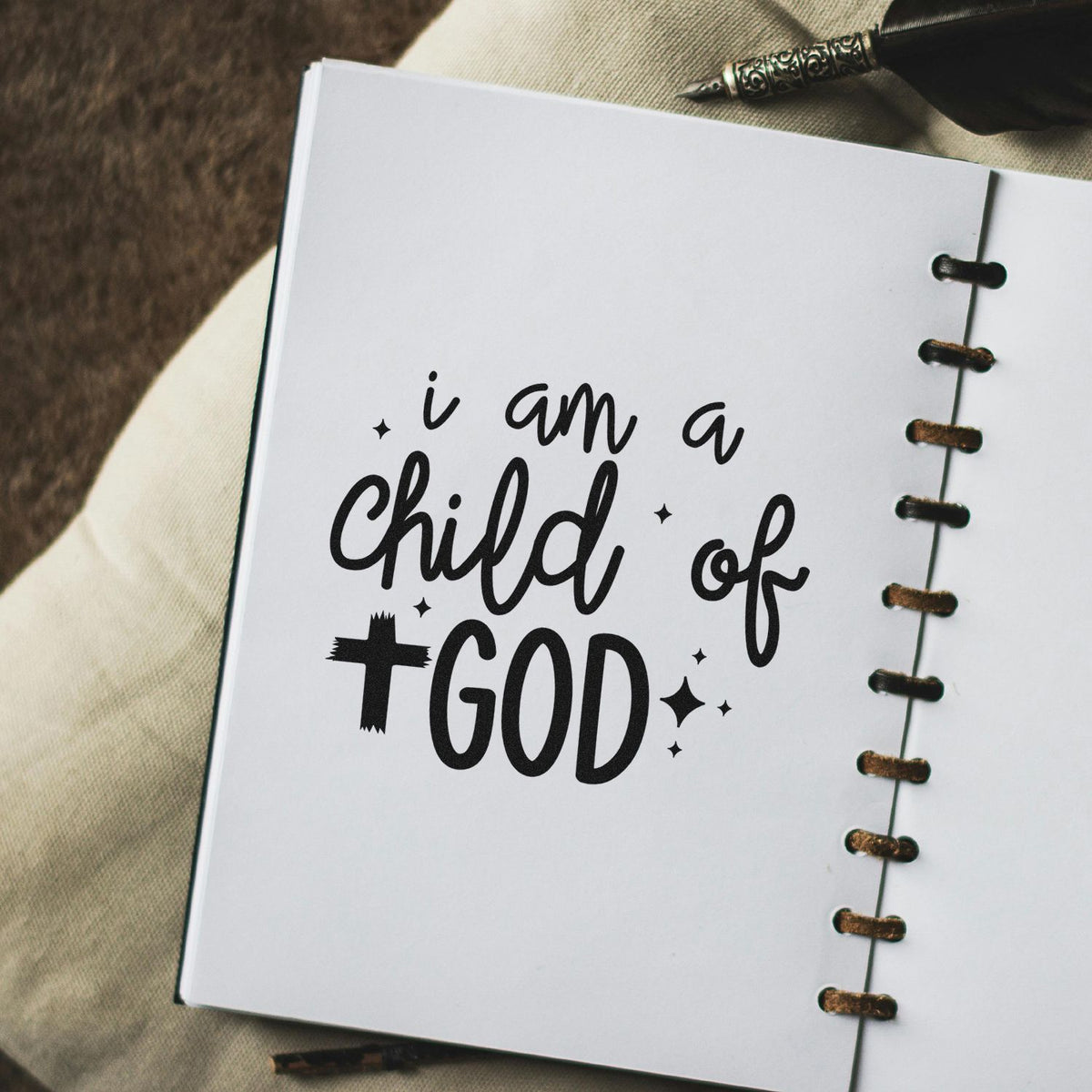 Black faith stamp seal reading I am a child of GOD on a white notebook page with brown binding and pen.