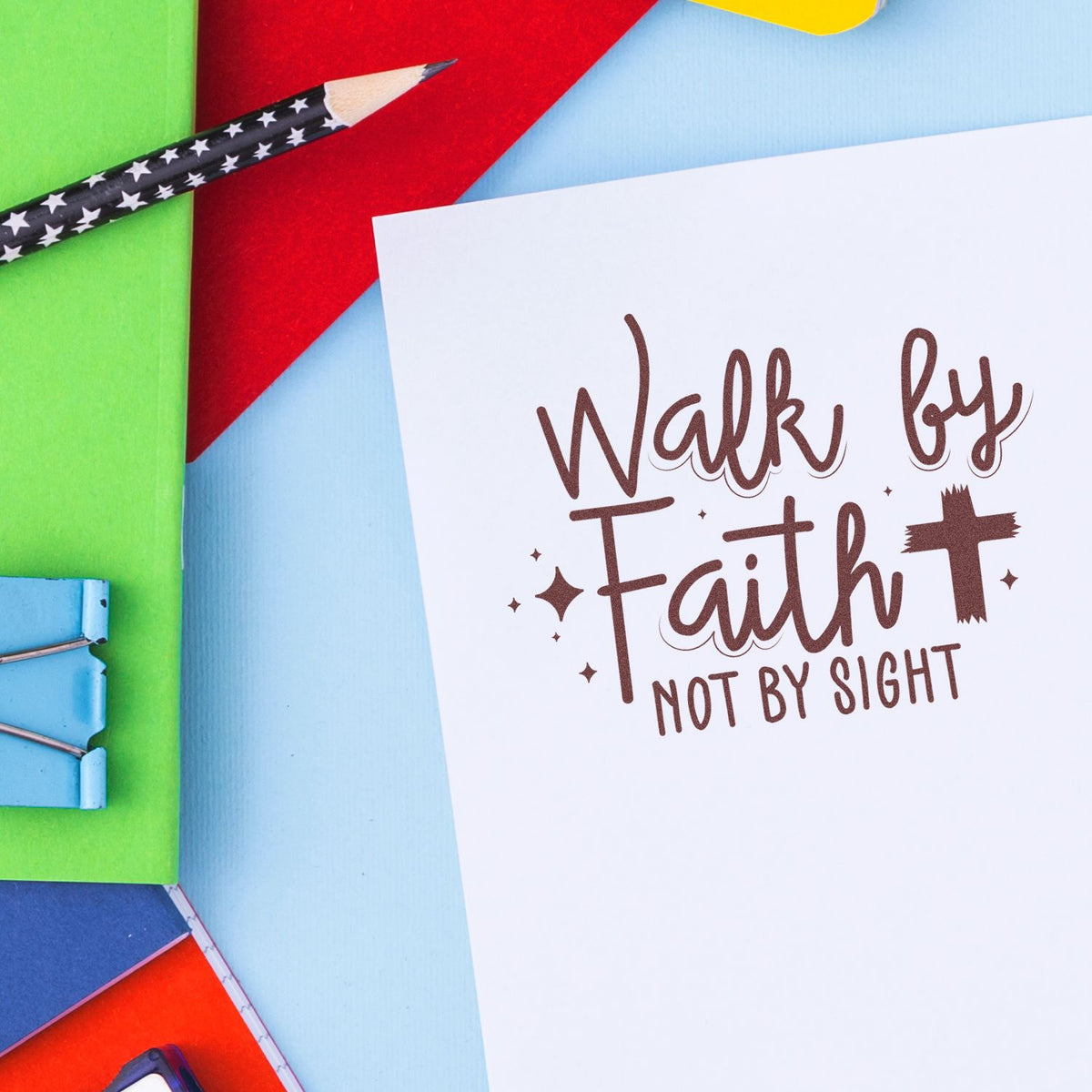 White stamp and seal design with brown Walk by Faith, Not by Sight text, colorful paper, pencil, and binder clips.