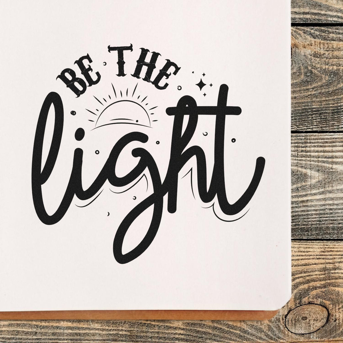 Black custom stamp seal reading Be The Light with sunrise, stars, and flowing script on white paper.