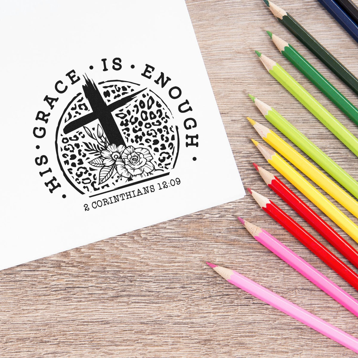 Black Grace Is Enough stamp and seal design on white paper beside colorful pencils on a wood surface.