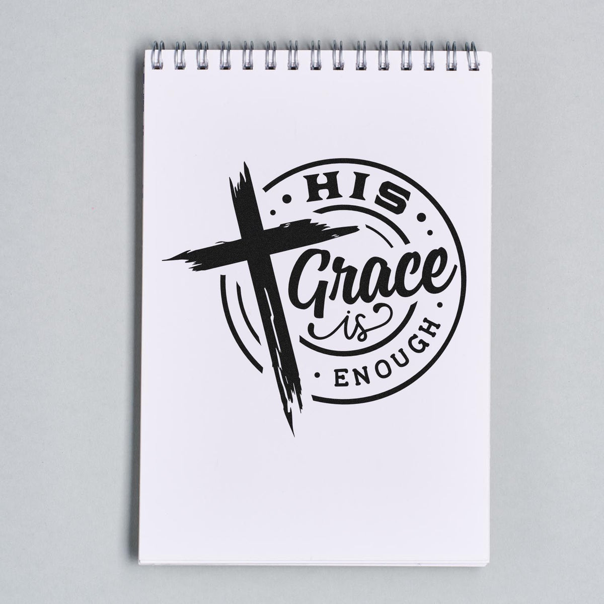 Black custom stamp seal with cross and His Grace is Enough on a white spiral notepad.