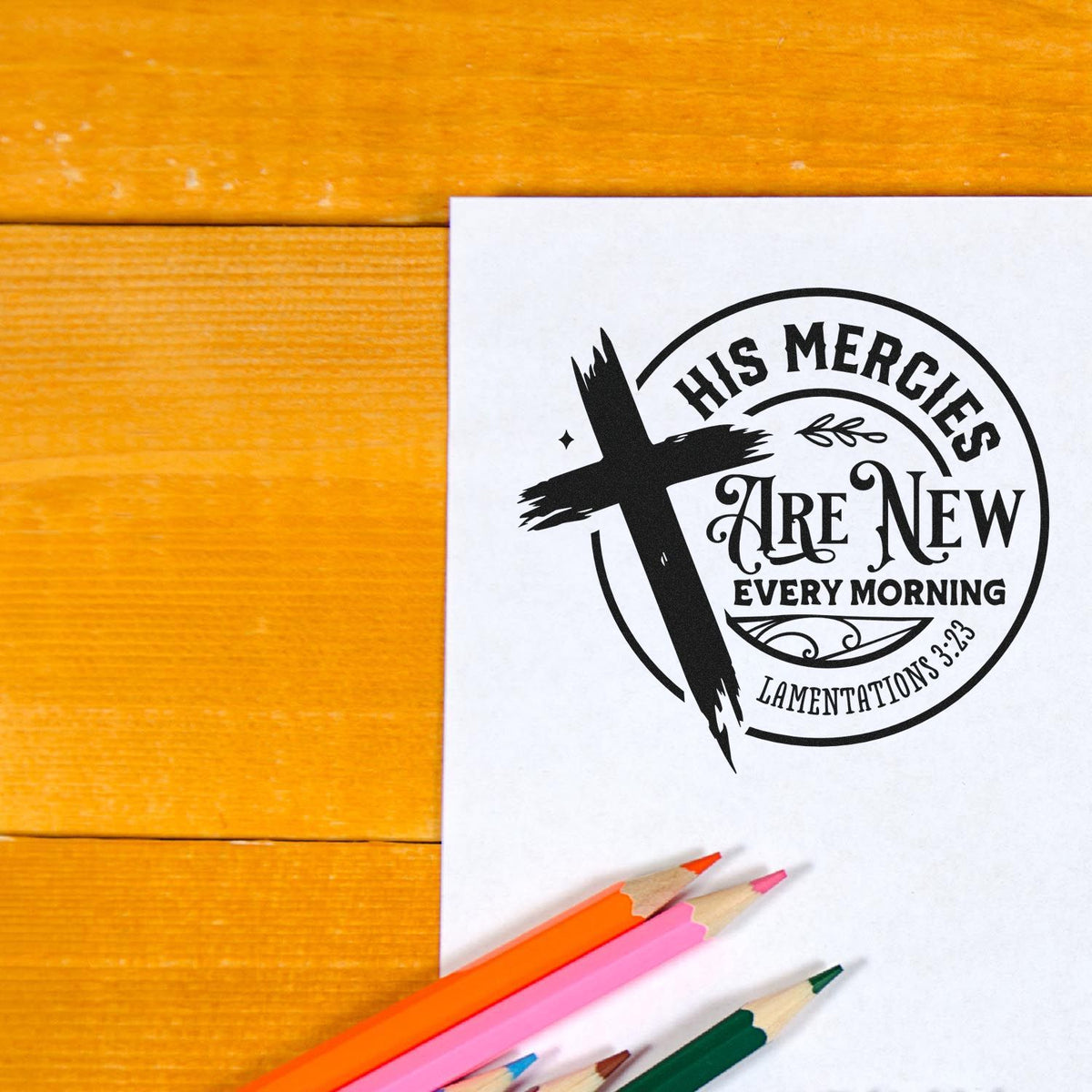 Black religious stamp seal with cross and His mercies are new every morning on white paper, with colored pencils on orange wood.