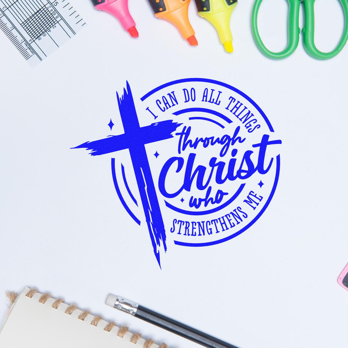 Blue Christian stamp and seal design with cross and quote on white, surrounded by colorful craft tools.