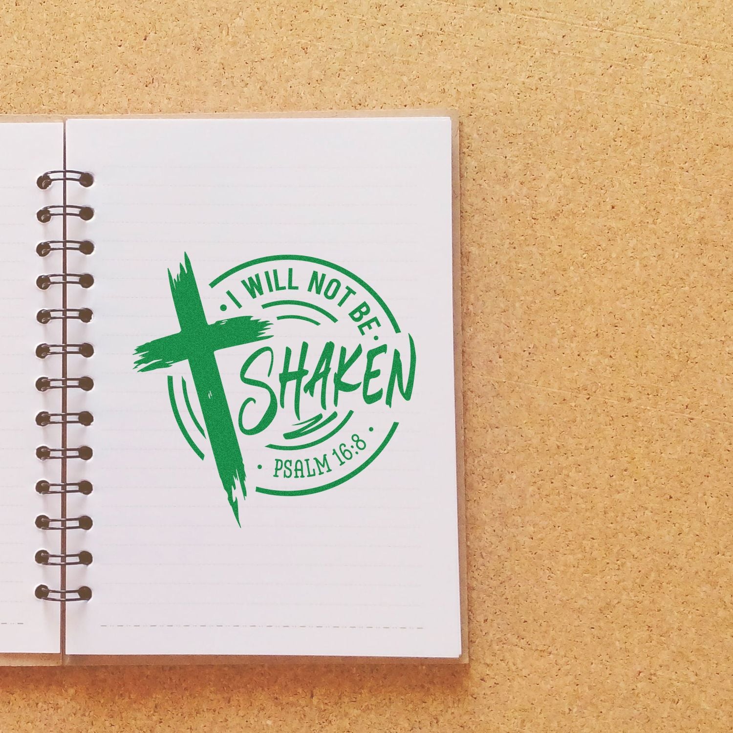 Green Christian stamp seal reading I Will Not Be Shaken with cross and Psalm 16:8 on a lined spiral notebook.
