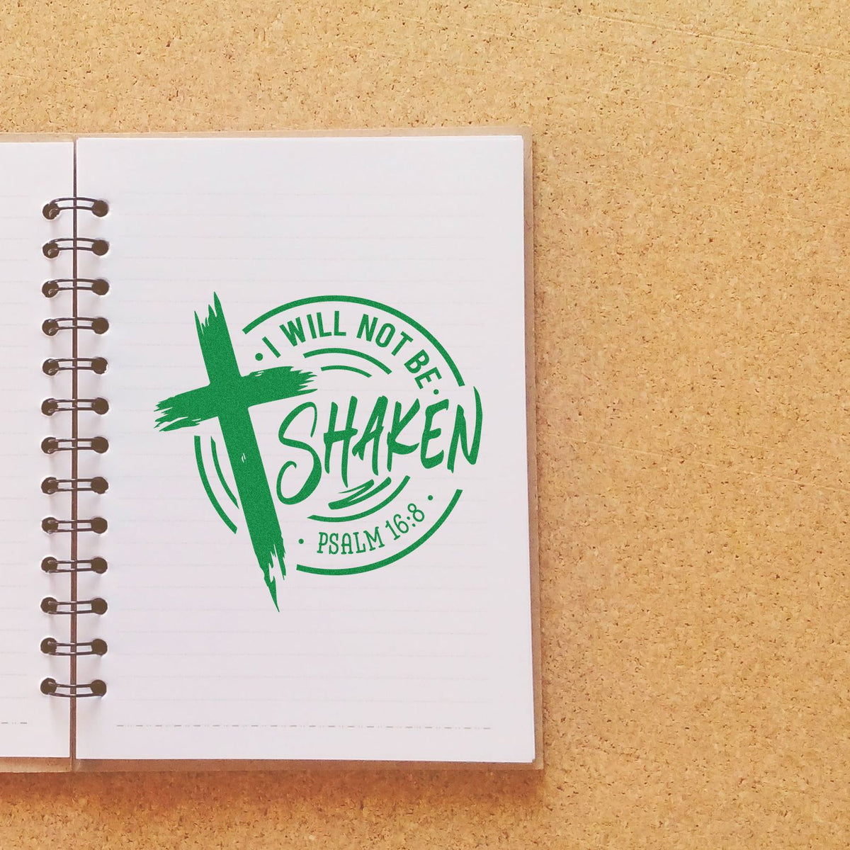 Green Christian stamp seal with cross, I WILL NOT BE SHAKEN and Psalm 16:8 on a white notebook.