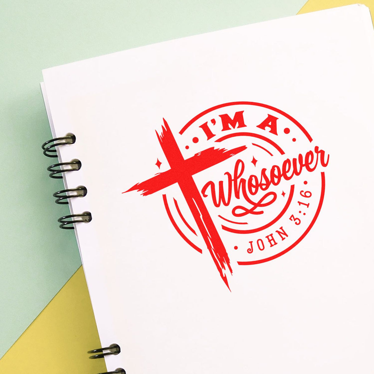 Red Christian stamp seal reading Im a Whosoever John 3:16 on white spiral notebook, with pastel green and yellow background.