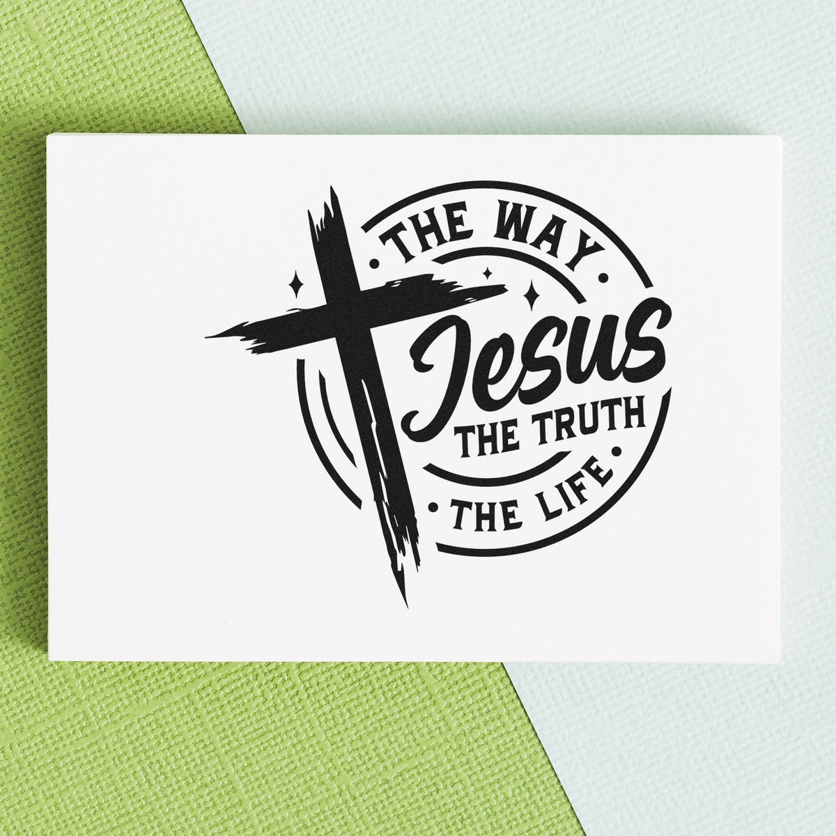 Black stamp seal with cross and The Way Jesus The Truth The Life on white card over green and white textured background.