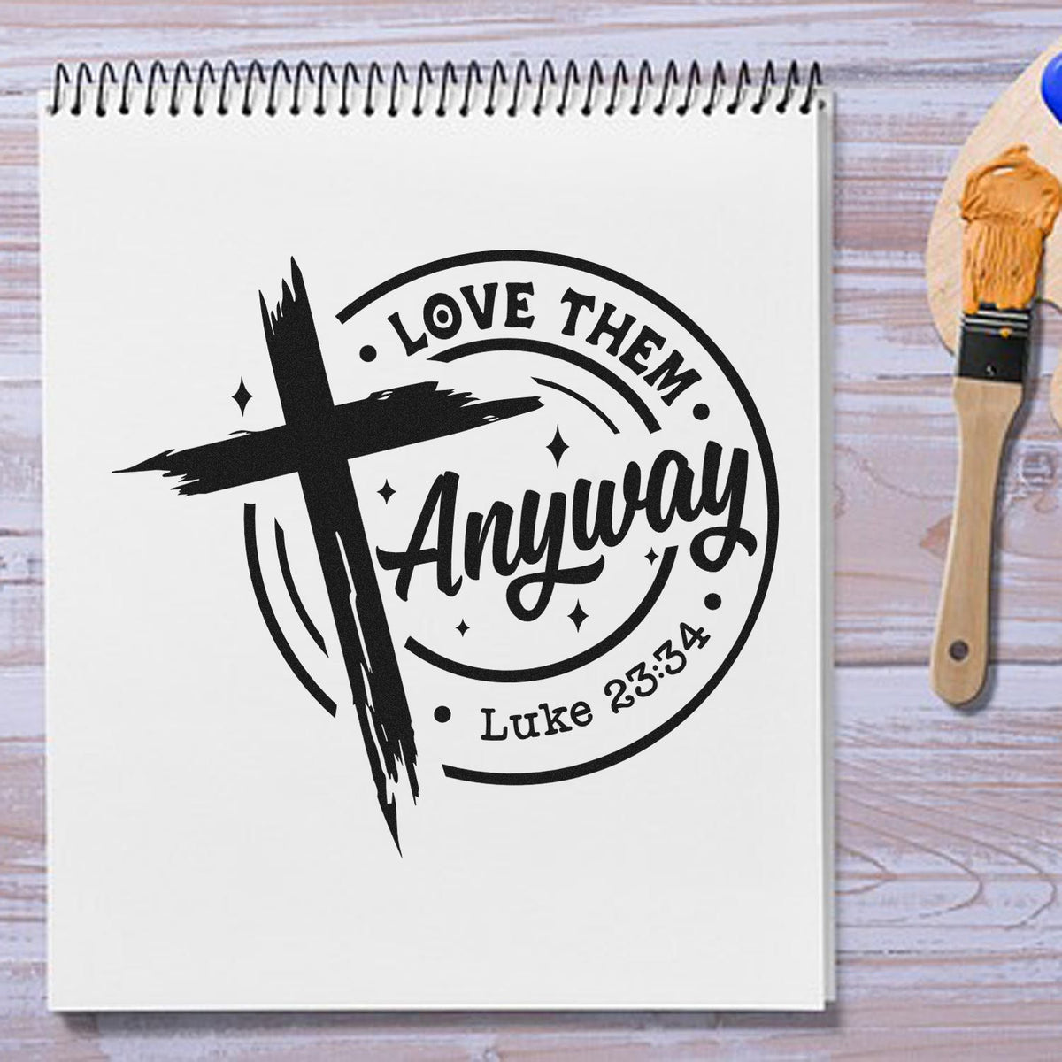 Black Christian rubber stamp seal with cross and Love Them Anyway Luke 23:34 on a white spiral notebook