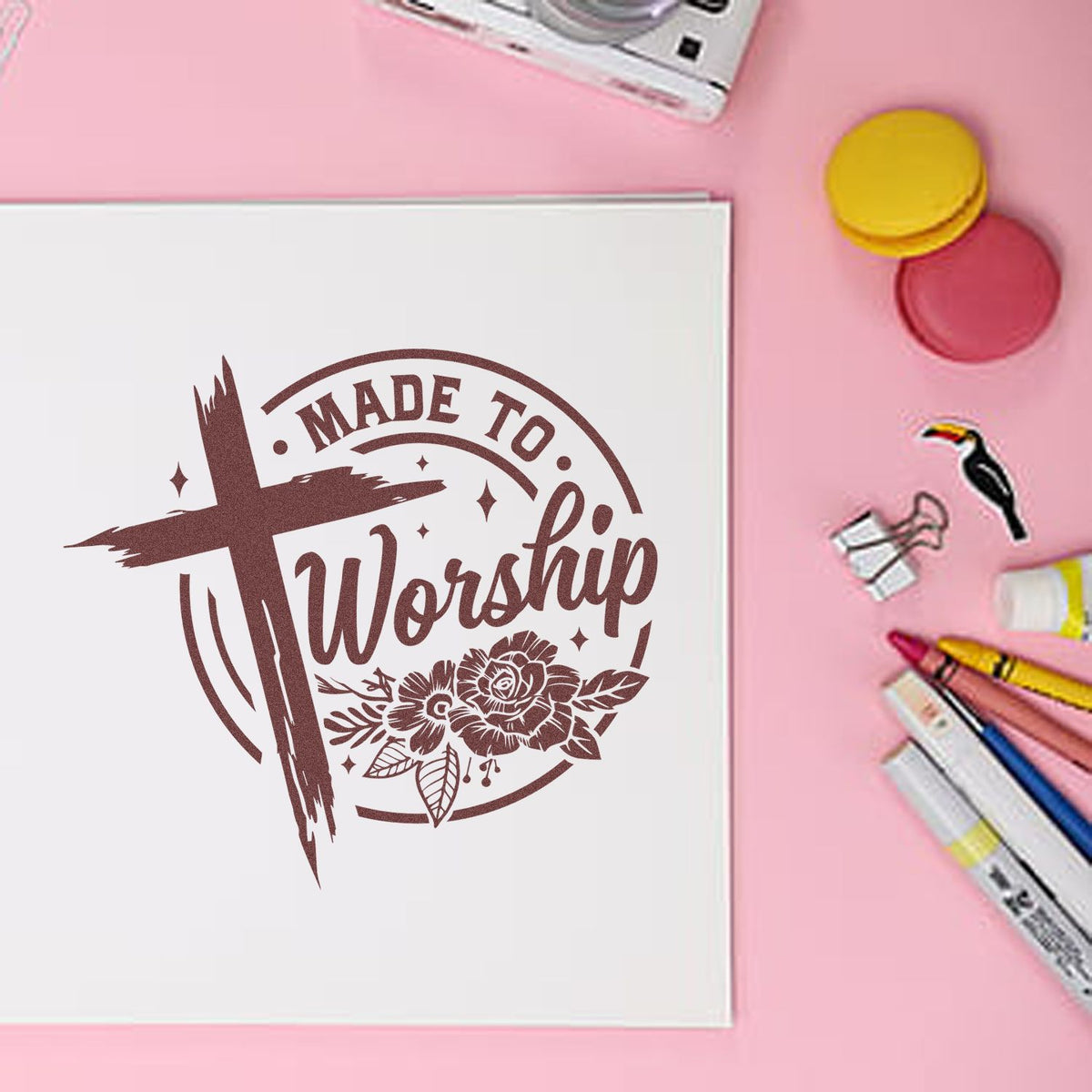 Brown Made to Worship stamp and seal design with cross and floral accents on white paper against a pink background.