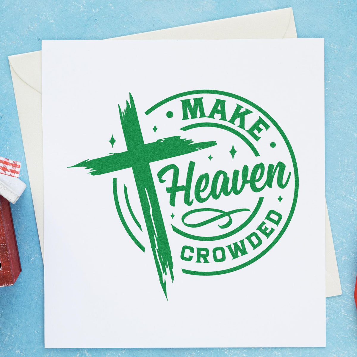Green Make Heaven Crowded stamp seal with cross graphic on a white card, set on a light blue background.