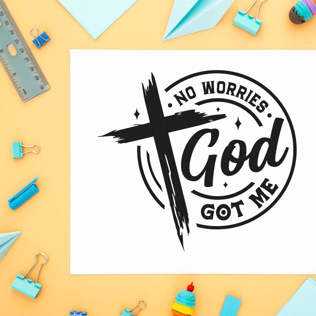 Black circular faith stamp seal reading No Worries God Got Me on white paper, surrounded by pastel stationery and clips.