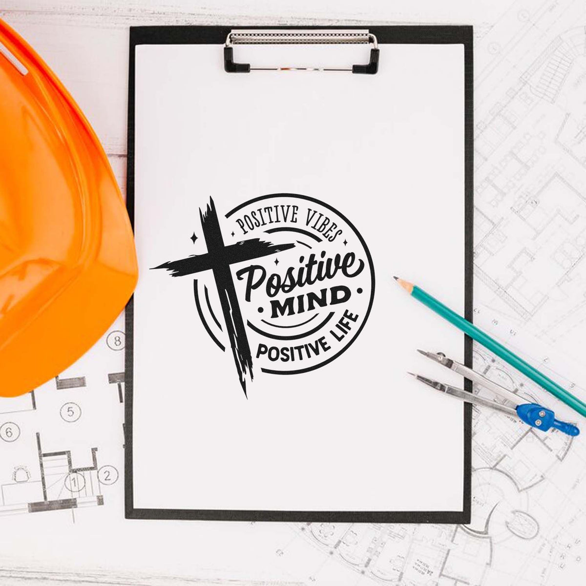 Black motivational stamp seal on a clipboard with orange hard hat, pencils, and blueprint sketches.