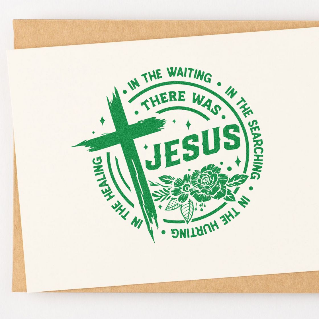 Green Christian stamp seal with cross, JESUS text, and floral design on cream paper over kraft envelope.