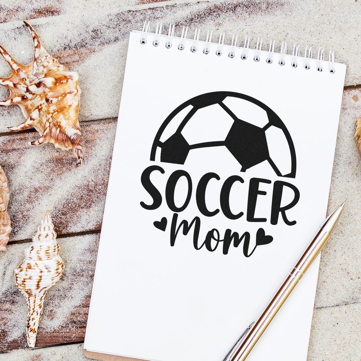 Black soccer mom stamp and seal design on white spiral notebook, with seashells and gold pen.