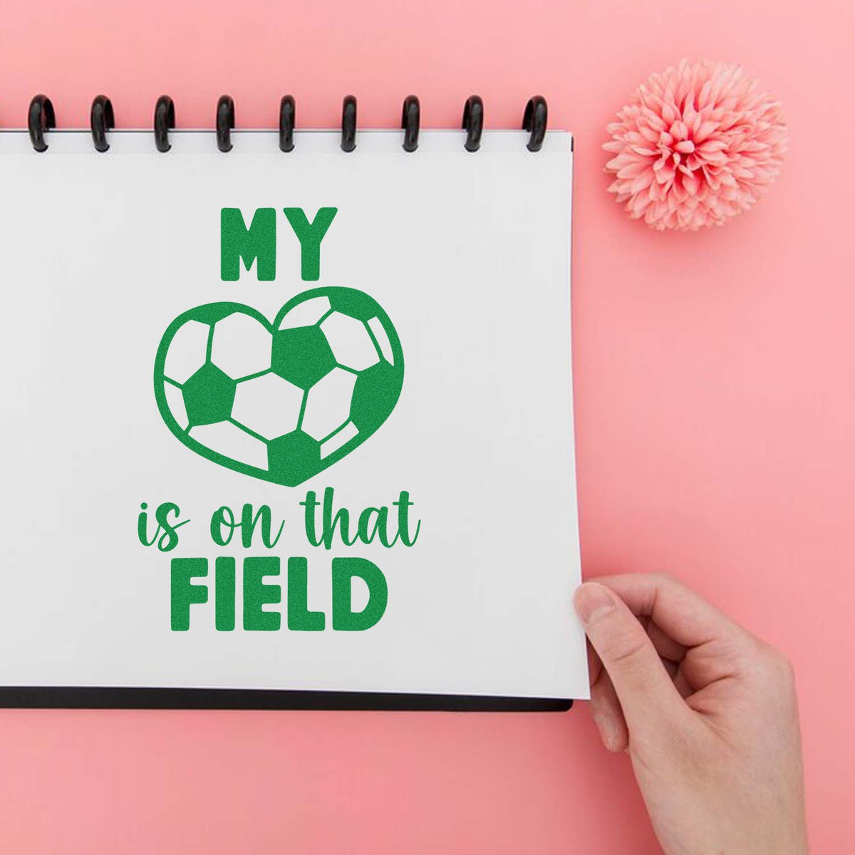 Green soccer-ball heart stamp and seal on a white notebook page reading My heart is on that field, with a pink backdrop.