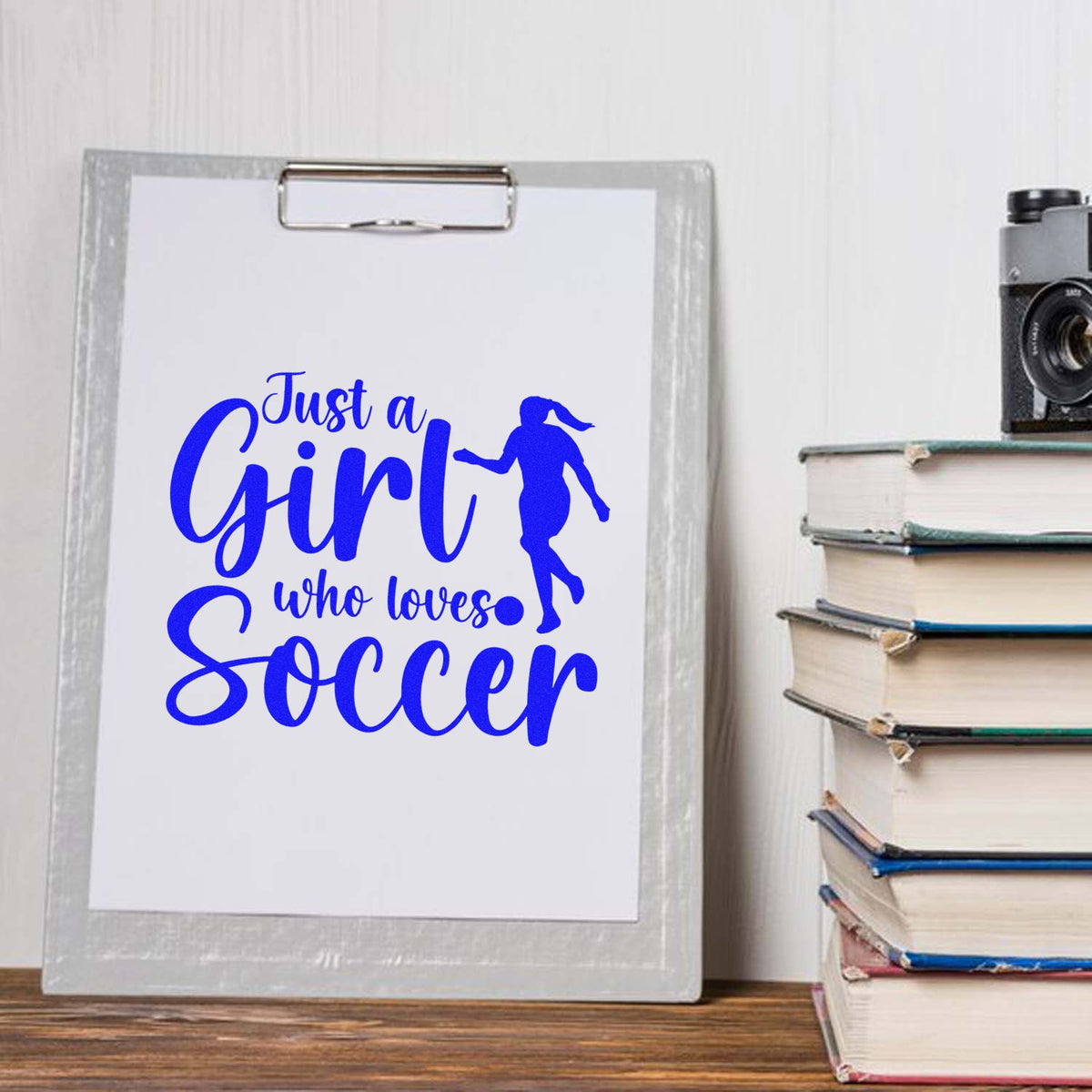 Blue soccer-themed stamp/seal design on clipboard reading Just a Girl who loves Soccer with girl silhouette.