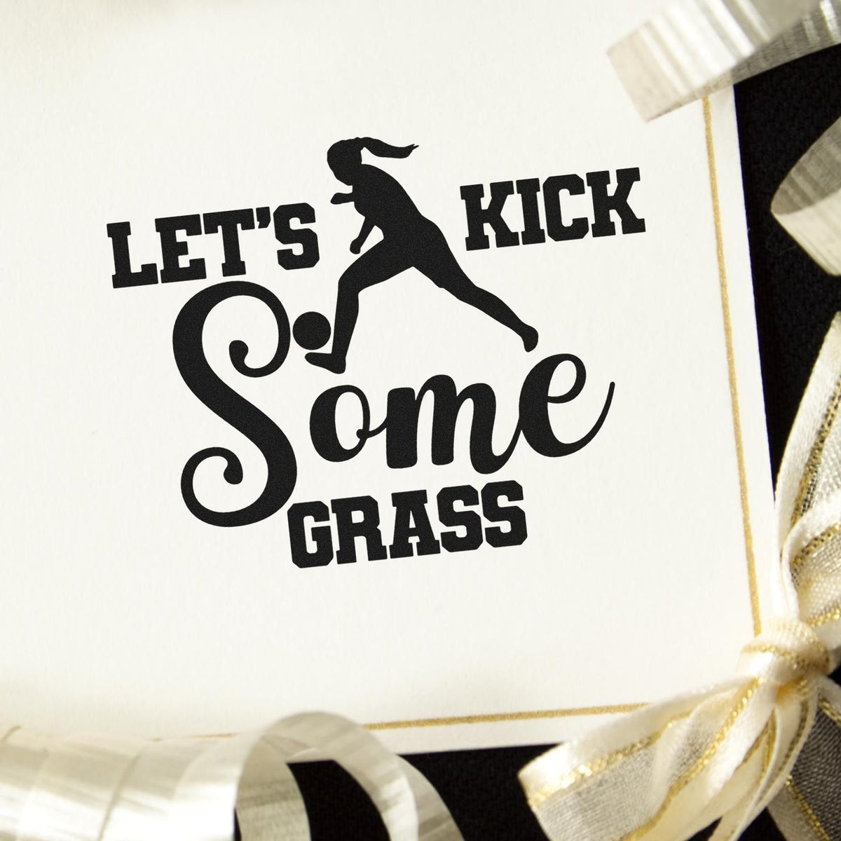 Black custom stamp seal with soccer player silhouette and Lets Kick Some Grass on a white card, accented by gold ribbon.
