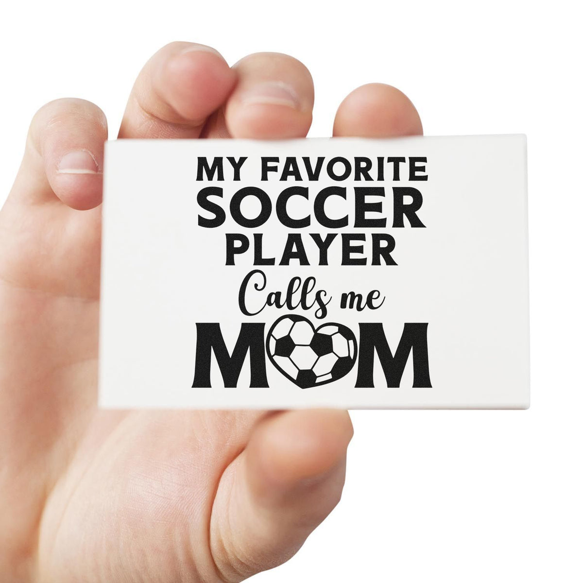 Hand holding a white stamp seal with black text, My favorite soccer player calls me mom, and a soccer ball heart.