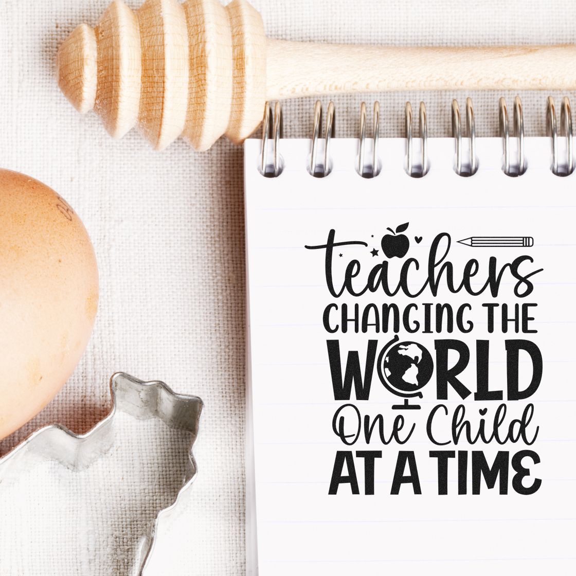 Black teacher appreciation stamp on white spiral notebook, with wooden seal stamp tool, apple, and pencil accents.