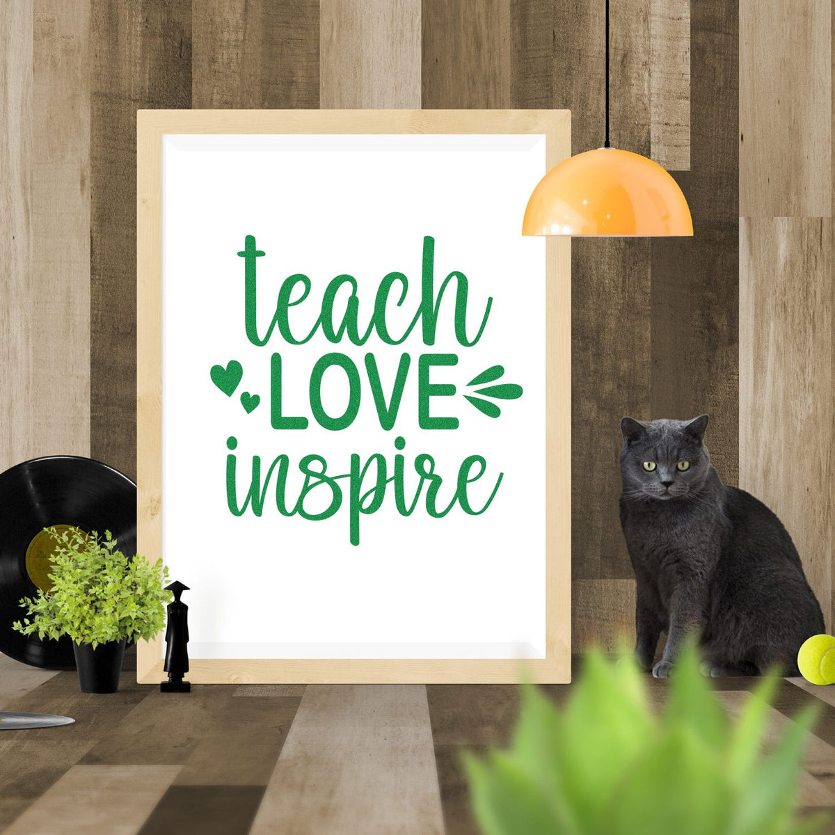 Stamp and seal product design with green teach LOVE inspire text in a wood frame, plus orange lamp, black cat, and plants.