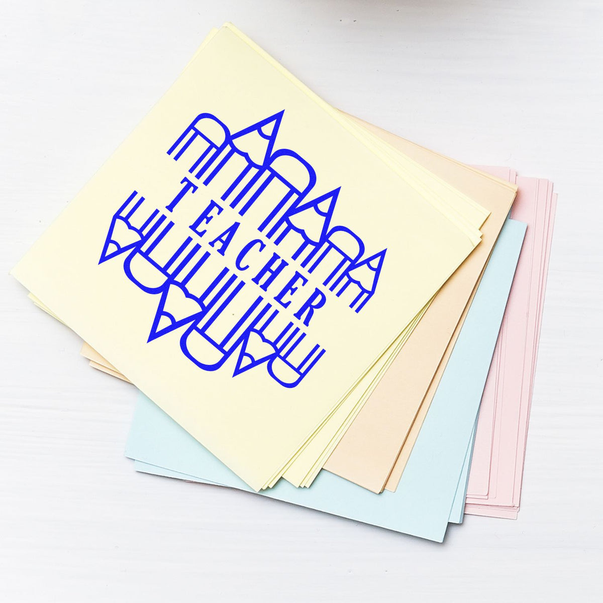Cream, pink, and blue paper stack with bold blue Teacher stamp and pencil seal design.