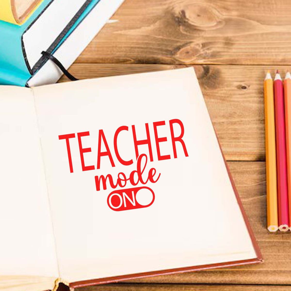Red teacher mode ON stamp and seal on open notebook beside colored pencils on a wooden desk.