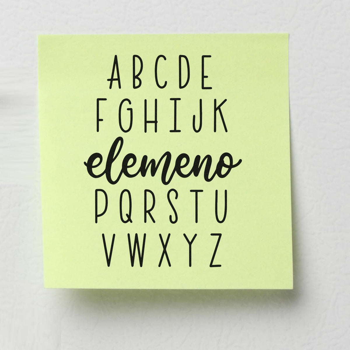 Pale yellow alphabet stamp and seal block with black A-Z letters and cursive elemeno centered.