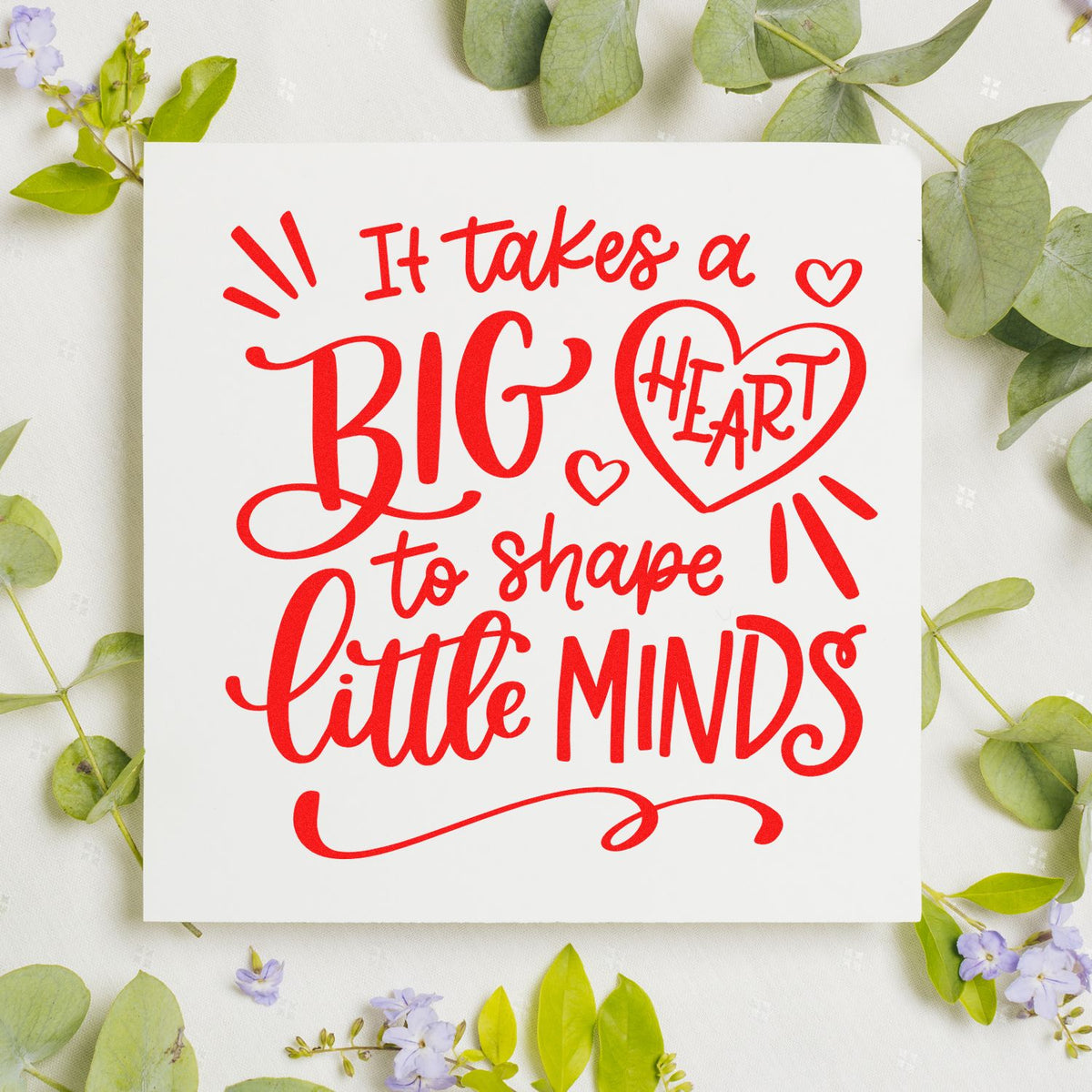 Red stamp and seal design reading It takes a big heart to shape little minds on white, framed by green leaves and lavender flowers.