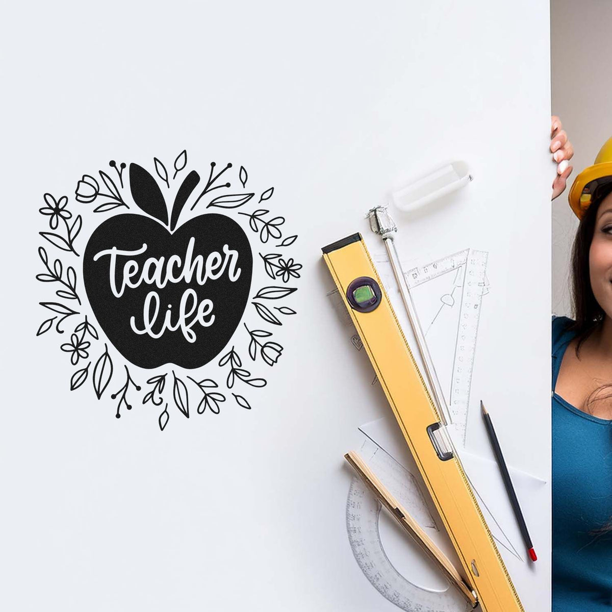 Black apple-shaped teacher life stamp seal with floral outline, beside yellow drafting tools on a white background.