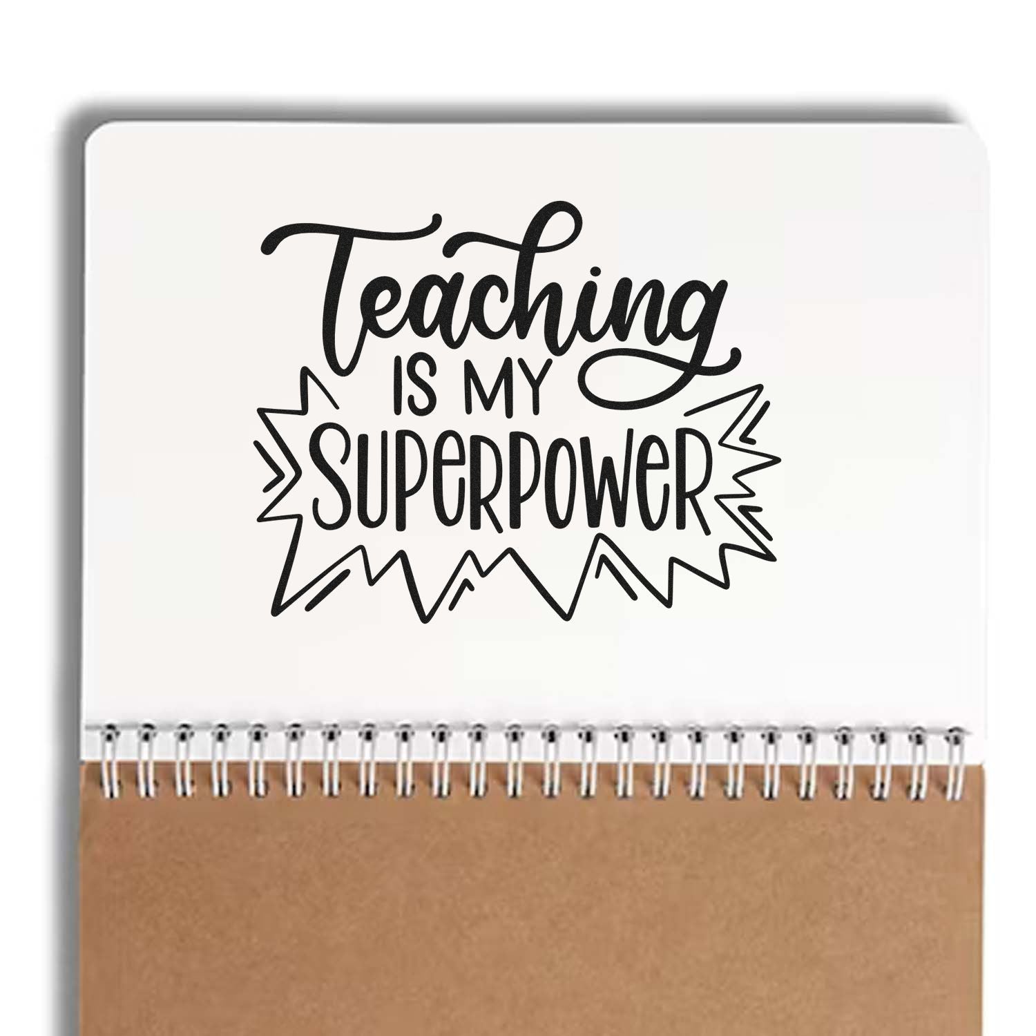 Black teaching stamp/seal with Teaching is my superpower on a white spiral notebook, brown cover.