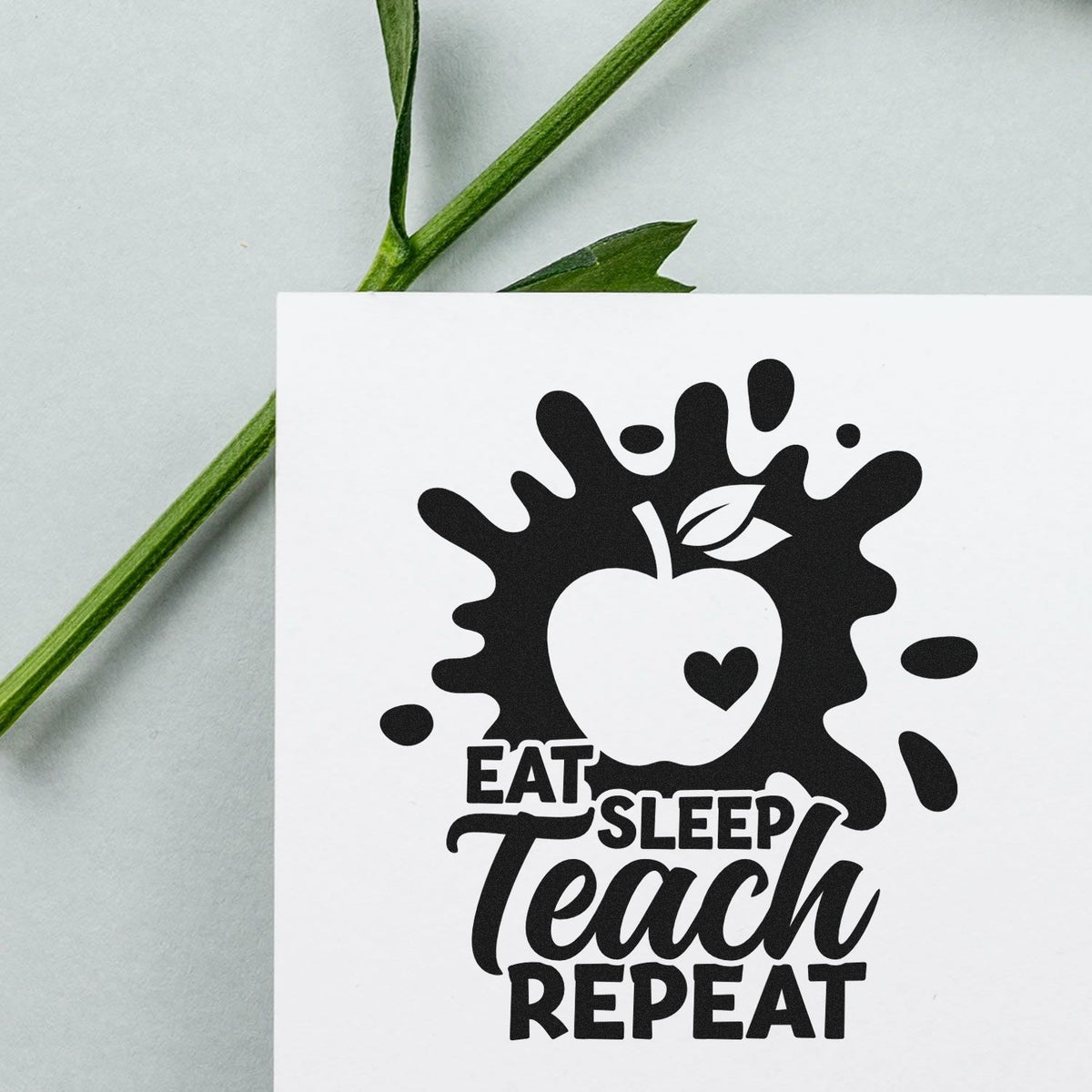 Black teacher stamp and seal design with apple splash and heart, reading Eat Sleep Teach Repeat on white card.