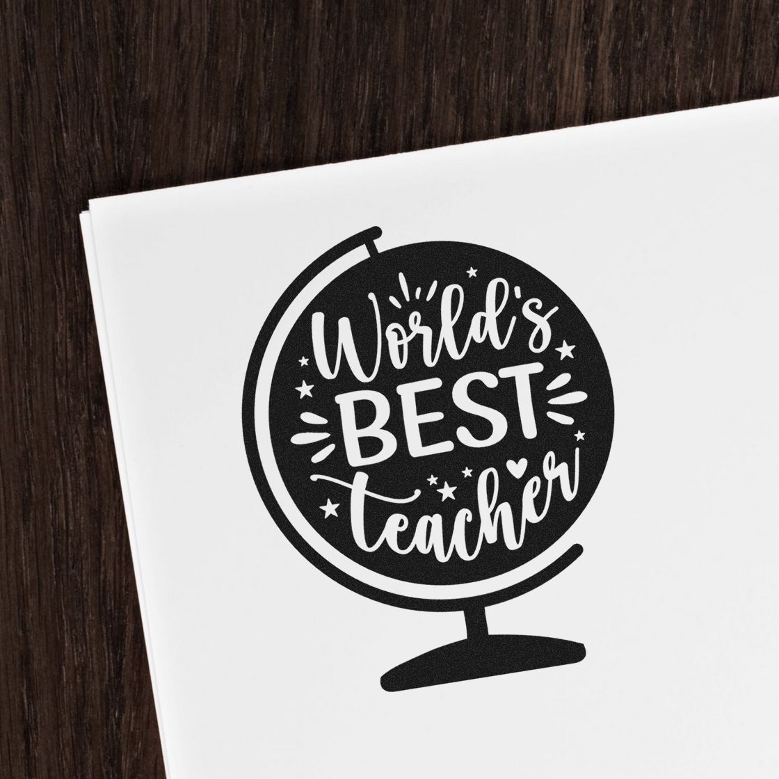 Black World's Best Teacher globe stamp seal on white paper, with stars, heart, and dark wood background.