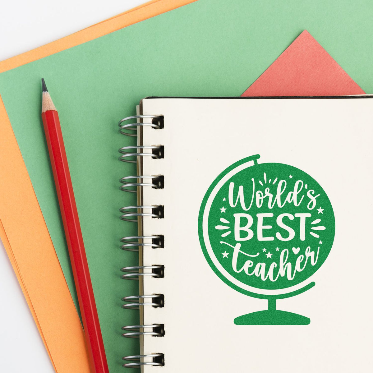 Green teacher stamp seal on a spiral notebook, with a red pencil and colorful paper background.