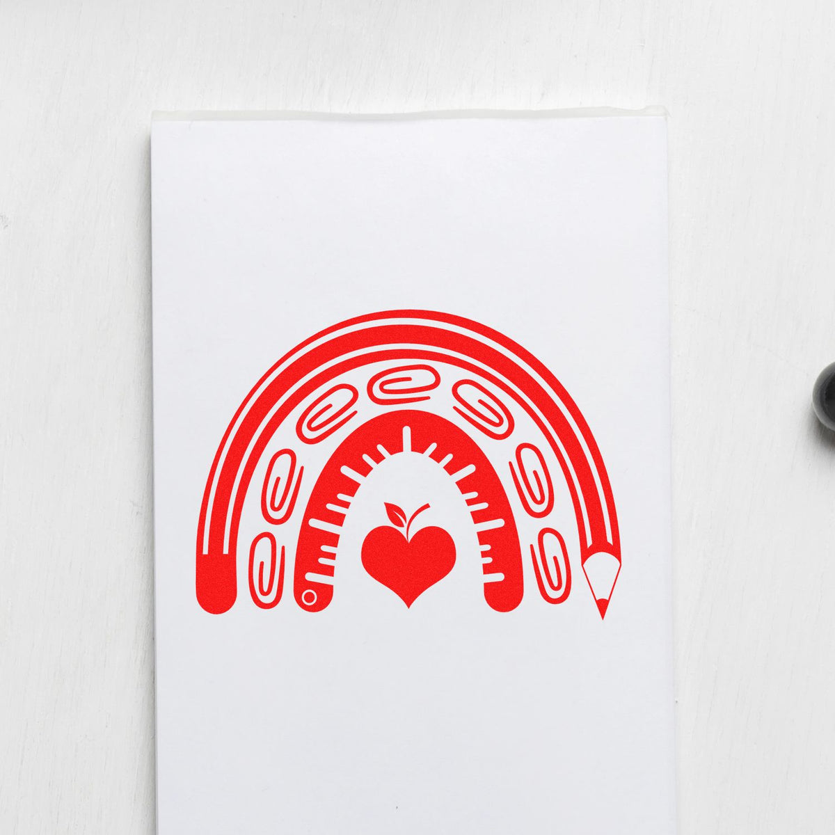 Red stationery stamp seal with rainbow pencil, paper clips, ruler, and heart on white paper