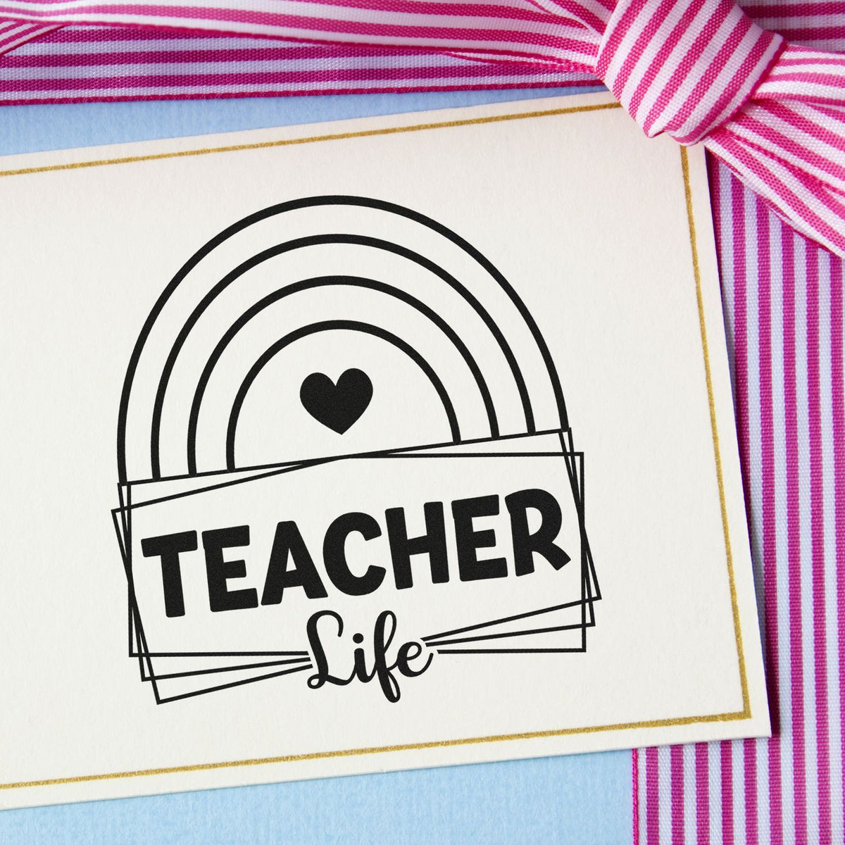 Black Teacher Life stamp seal with rainbow heart on white card, gold border, pink striped ribbon, and blue background
