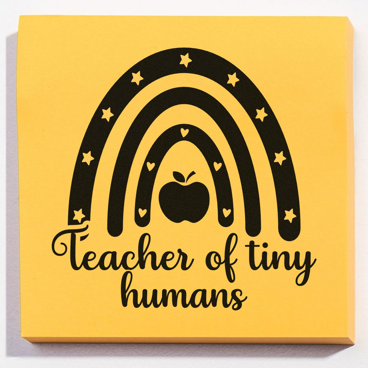 Yellow stamp seal with black rainbow, stars, hearts and apple; Teacher of tiny humans text.