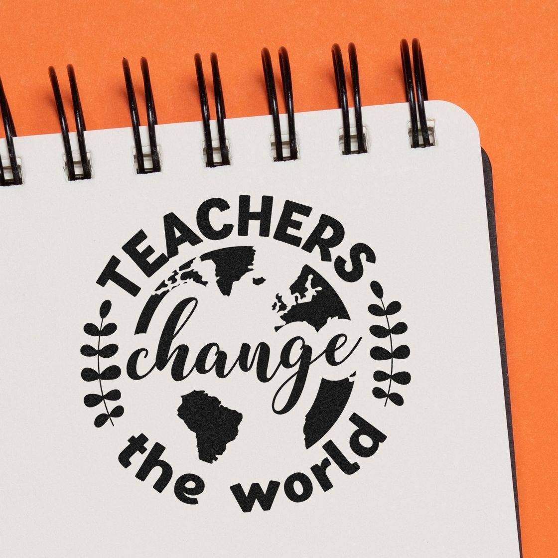 Black rubber stamp design reading Teachers change the world with globe and leaves on white notebook, orange background.