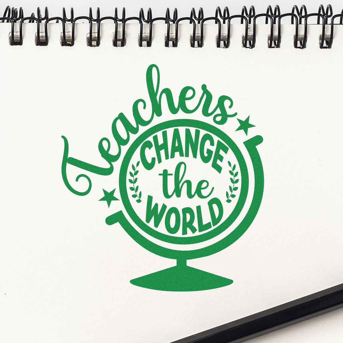 Green globe-shaped stamp seal reading Teachers Change the World on a white spiral notebook.