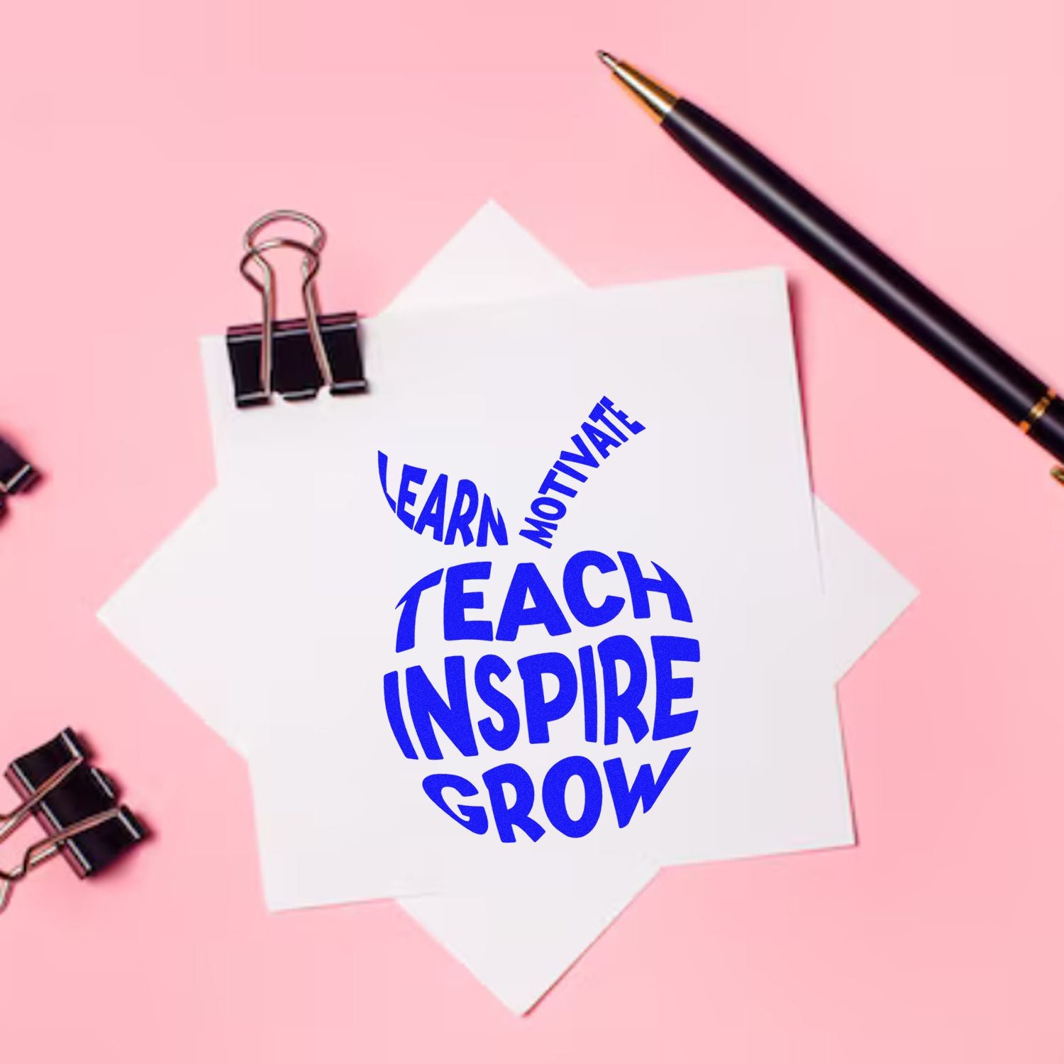 Blue teacher stamp seal reading Teach Inspire Grow on white paper, with black pen and binder clips on a pink background.