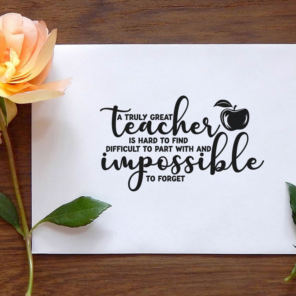 Black teacher quote stamp seal on white paper, with apple icon, peach flower, green leaves, and wood background.
