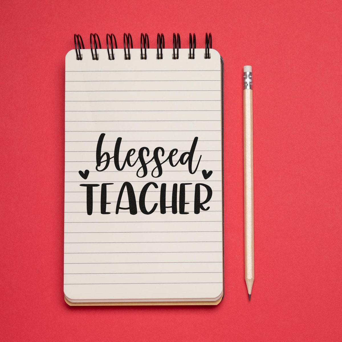 Blessed Teacher stamp/seal on lined notebook with pencil, set on a bright red background.