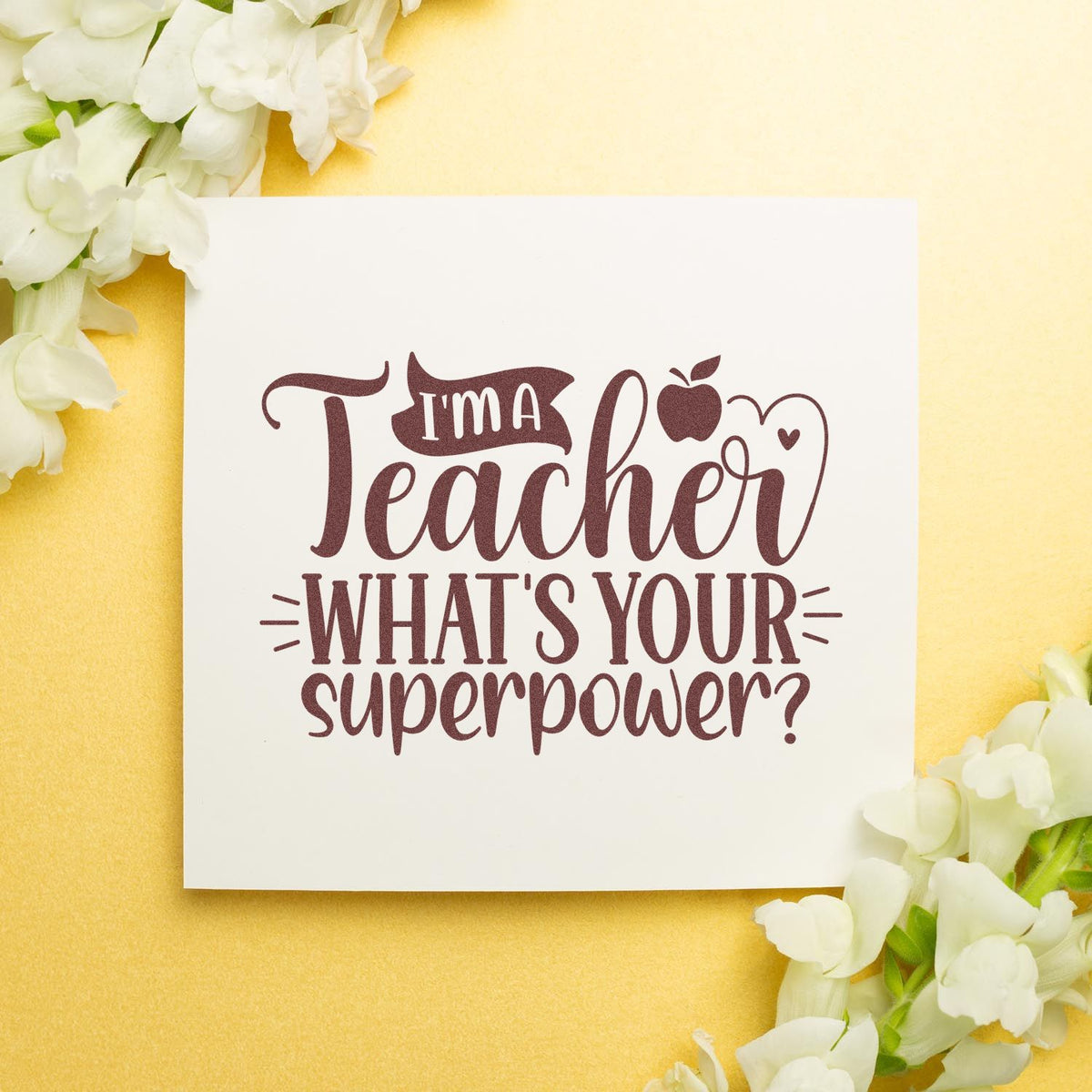 Maroon teacher stamp and seal on white card, reading Im a Teacher, Whats Your Superpower? with white flowers on pale yellow background.